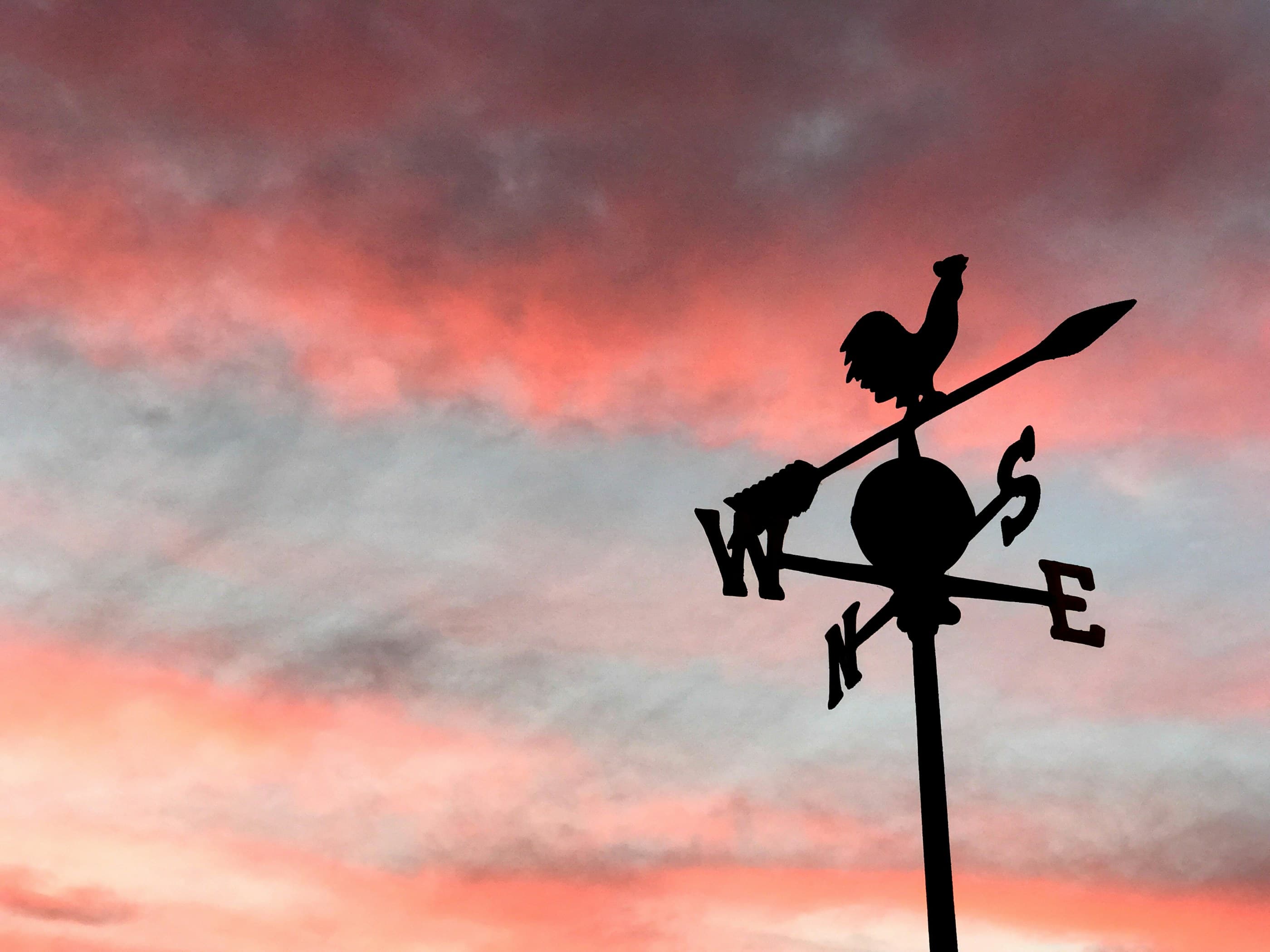 A black arrow weathervane against a pink evening sky